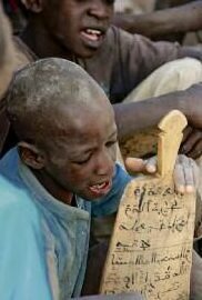 Elève dans une école coranique avec une tablette d’alphabet arabe